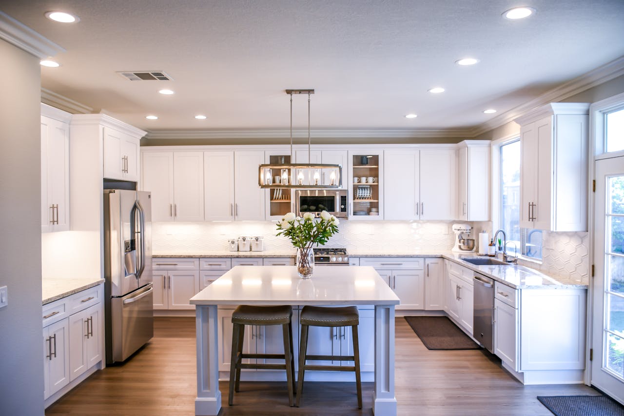 about-us Spacious and elegant kitchen featuring white cabinetry, island, and stainless steel appliances.